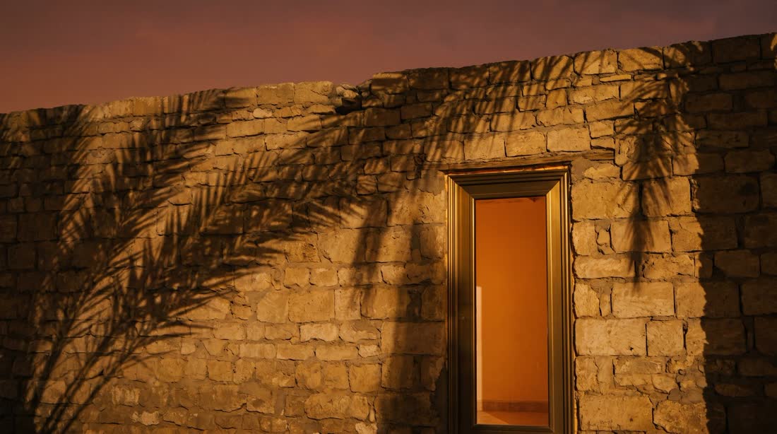 Limestone wall at dusk with palm shadows and a glowing doorway